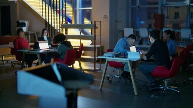 A diverse team of professionals works late into the night in a modern, open-plan office space. Dedicated colleagues collaborate on laptops and projects, showcasing their commitment to business.