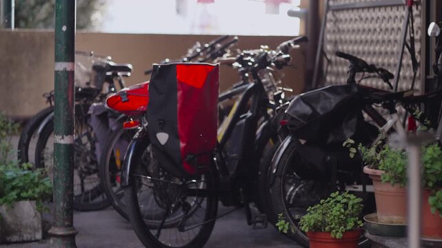 Urban courtyard filled with parked bicycles equipped with colorful bags and surrounding potted plants creating peaceful functional scene blending transportation storage