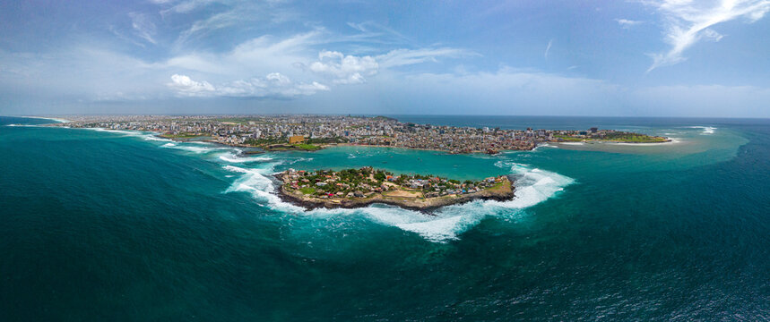 Aerial view of Ngor Island surrounded by turquoise ocean waves with the city skyline in the background in Dakar, Dakar Region, Senegal.