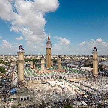Aerial view of the Great Mosque of Touba featuring its tall minarets and a crowded courtyard under a blue sky with white clouds in Touba, Diourbel Region, Senegal.