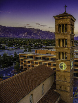 Aerial view of St. Andrew Catholic Church bell tower and its illuminated clock face with the San Gabriel Mountains at dusk in Pasadena, California, United States.
