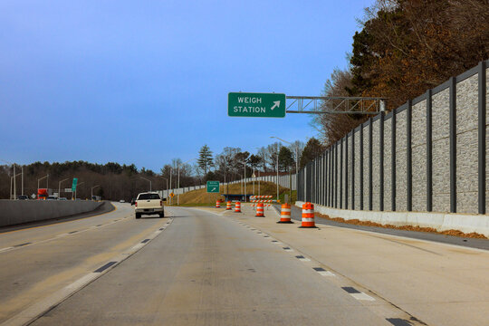Truck vehicles drive on highway near weigh station with construction barriers visible on side.