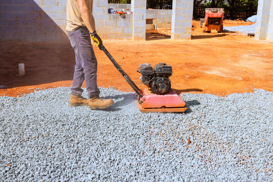 Worker operates plate compactor on gravel at construction site