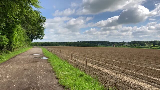 Agricultural field in the rural countryside and metal fence barrier, tilled and prepared for planting crops, muddy ground or soil with furrows and tractor tire tracks in Germany, Europe