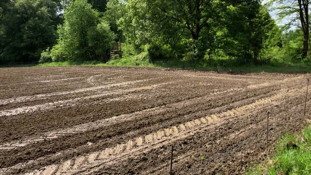 Agricultural field in the rural countryside and metal fence barrier, tilled and prepared for planting crops, muddy ground or soil with furrows and tractor tire tracks in Germany, Europe