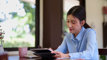 young Asian women working at cafe using tablet computer browsing internet reading digital content at coffee shop near window with natural light morning © Pichsakul