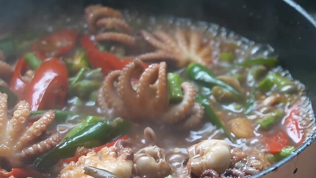 Close-up of spicy stir-fried baby octopus with red and green chili peppers cooking in a hot pan, authentic Asian seafood dish