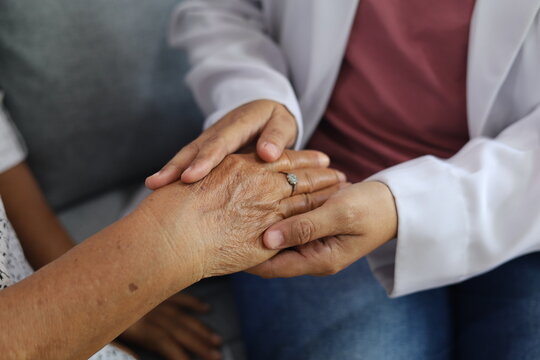 Arthritis or parkinson disease elderly patient, old aged senior woman holding geriatric doctor, cargiving nurse or family assistant's hand in hospice home for medical health care or mental therapy