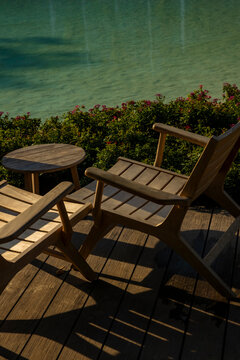Wooden chairs and table by tropical resort water, peaceful outdoor relaxation area. Concept: slow living.
