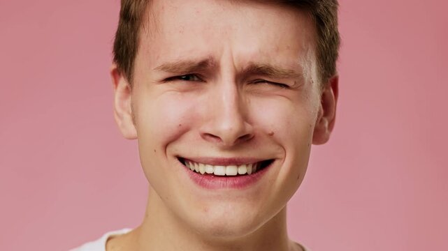 A young man with light skin is showing a surprised or confused expression in front of a pink backdrop. He has short brown hair and wears a simple white shirt.