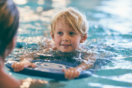 Child learning to swim with a kickboard during a supervised pool lesson, representing water safety, swim education and confidence in the water