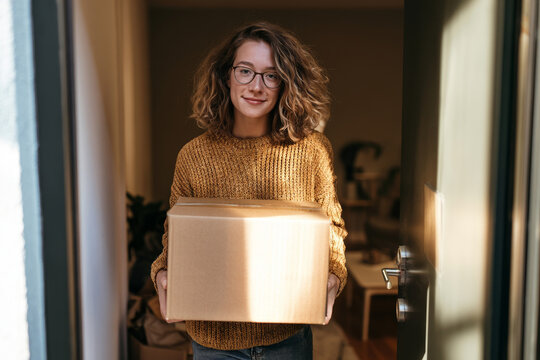 College student carrying a moving box into a dorm room or first apartment, representing student housing, moving out and the transition to independent living