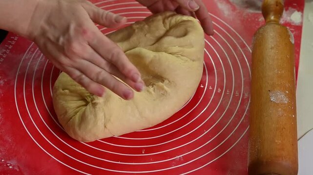 Dough kneading by hands on silicone mat during home baking. Dough pressed and folded repeatedly, It texture changing under fingers, closeup cooking process, homemade bread preparation concept.