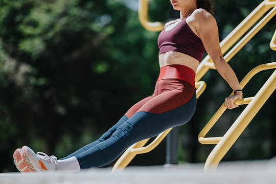 Woman in athletic wear performing a triceps dip on yellow outdoor fitness bars. Female exercising outdoors on parallel bars in a park setting for strength training.