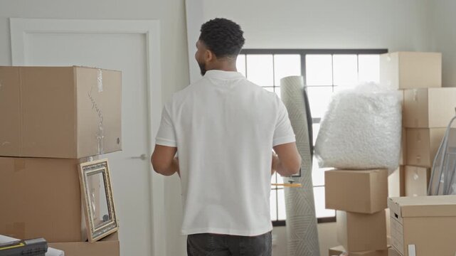Man holds medium cardboard box with both hands and smiles in a building entryway; moving day contentment.