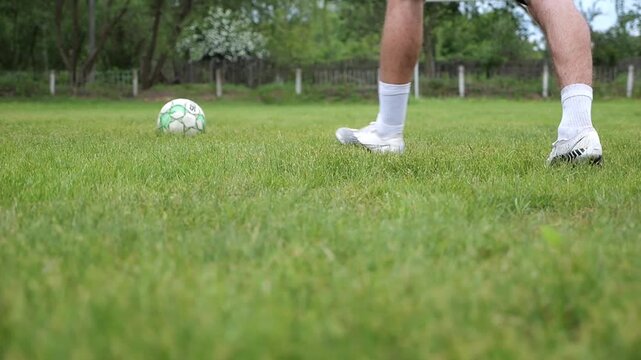 Leg of sportsman shooting a penalty kicks on stadium at summer day. Male foot of professional footballer kicking ball at green field. Young man training at meadow. Concept of a freestyle football