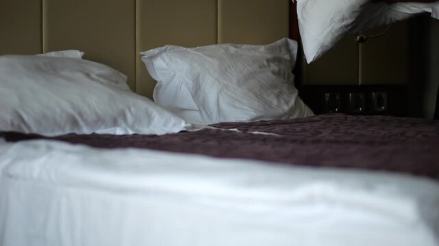 Male hands of maid adjusting pillow on a neatly made bed in a modern hotel room. Service personnel preparing clean bedding and comfortable accommodation for guests in hospitality interior. Slow mo
