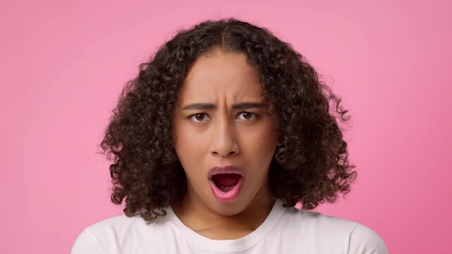 A woman with curly hair looks surprised with her mouth open against a bright pink background during a creative photo session. She expresses a strong emotion in a playful way.