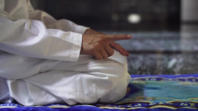 Muslim young man sitting in Tashahhud position during Salah prayer inside mosque.