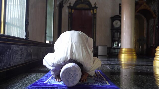 Devout Muslim man prostrating (Sujud) in prayer on a rug inside mosque.