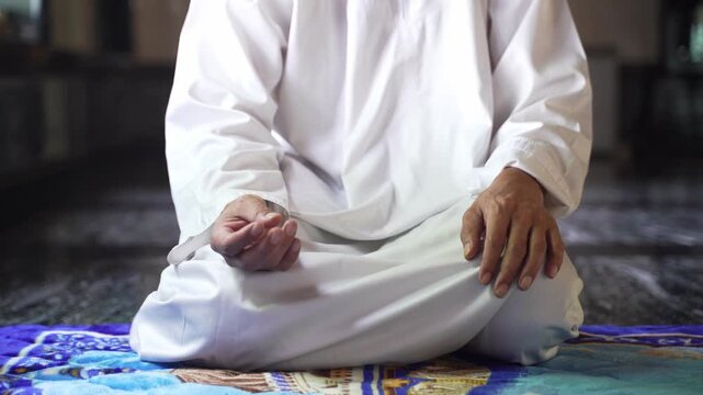 Muslim man holding and counting Islamic prayer beads (Misbaha) close up, spiritual devotion and faith inside peaceful mosque.
