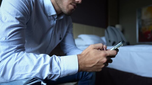 Male entrepreneur browsing modern smartphone while sitting in modern hotel room or apartment interior. Successful businessman using mobile technology showing communication and work routine. Slow mo
