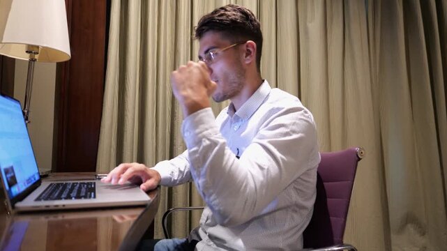 Young businessman working on laptop in modern hotel room and reacting to good news with excitement and happiness. Happy man celebrating success while using computer show achievement and motivation