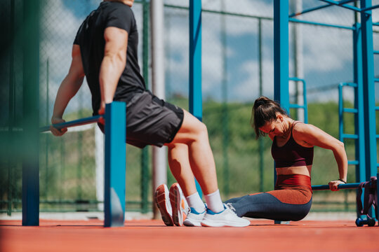 A man and woman perform bodyweight dips on parallel bars at an outdoor fitness park. The pair train calisthenics together, focusing on upper-body strength and core control.