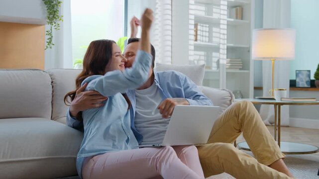 Joyful excited couple winning with laptop yelling happy hugging man kissing woman feeling happiness with online victory opportunity family win with computer receive good news notification at home