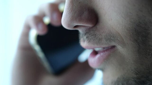 Close up male mouth speaking by smartphone near window with day light. Handsome bearded guy talking on phone at apartment. Young man having conversation on cellphone at office. Slow motion