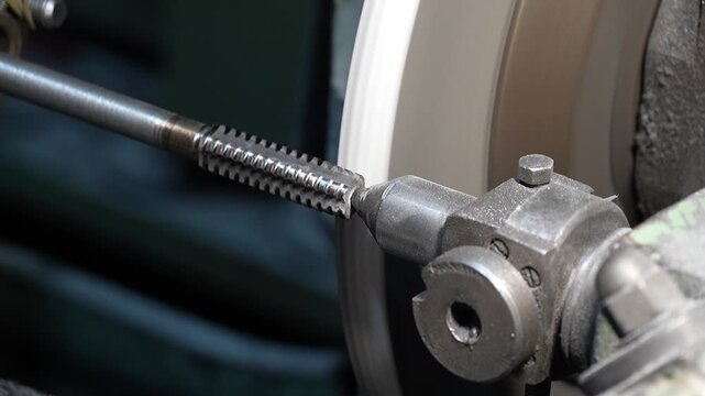 Close up of precision metal threading process on industrial grinding machine in workshop. Rotating steel rod and abrasive wheel during manufacturing operation show machining technology and engineering