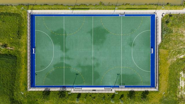 Aerial view of the H.C. Rijnvliet field hockey pitch featuring green turf and blue borders surrounded by lush grass in Utrecht, Utrecht, Netherlands.