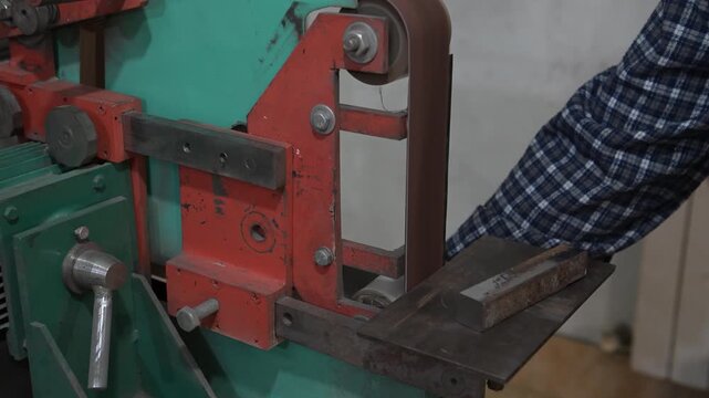 An electric machine for grinding metal in the production room of the workshop. The process of working and finishing on a metal-sanded grinding machine with working hands