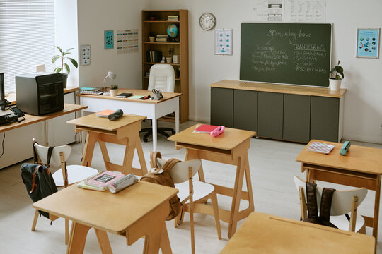 Wide angle shot of empty classroom showing student desks, teacher workspace, chalkboard lesson, learning setup for school education, academic planning, back to school marketing