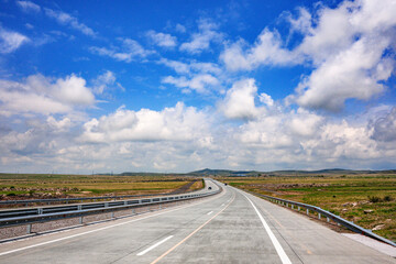 Obraz premium Open highway winds through vast grassy plains beneath cloudy blue sky