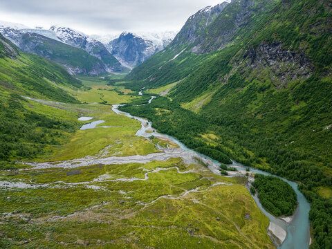 Aerial drone views of the tundra landscape in Jostedalsbreen National Park, where glacial rivers carve braided channels through a wide alpine valley in western Norway. The images capture the raw wilde