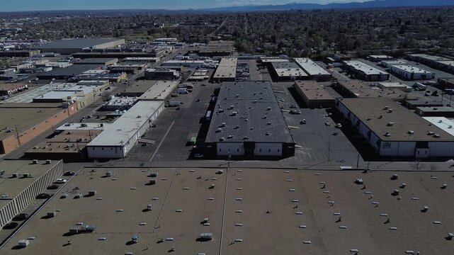 Industrial roof alignment highlighting rows of warehouses near W 4th Ave transitioning toward suburban housing distant foothills. Varied rooflines, rooftop units, sparse trees, fleet services, CO