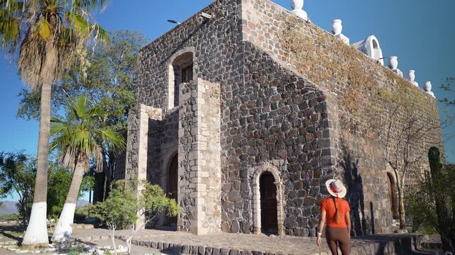 Mature woman visits Mission church Santa Rosalia in Mulege Baja California Sur. She walks through a lush oasis with palm trees.