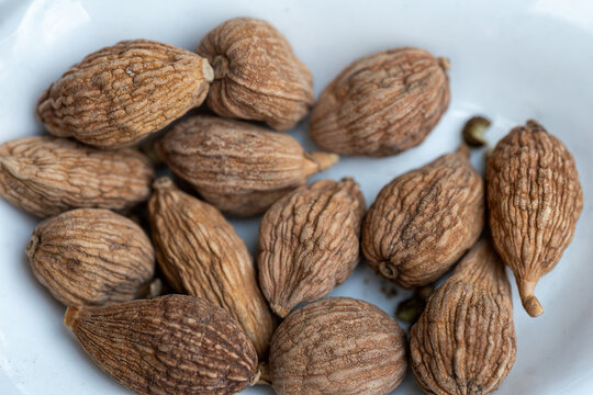 A cluster of dried Lanxangia tsaoko seeds sits on a white ceramic plate. These unique, fragrant seeds are traditionally used in perfumery and medicine, exhibiting a distinctive, woody aroma.