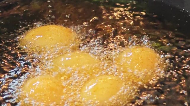 Macro shot of hard-boiled eggs deep frying in hot oil.