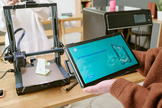 Close up of student using tablet for 3D printing workflow beside desktop printer, managing prototyping process