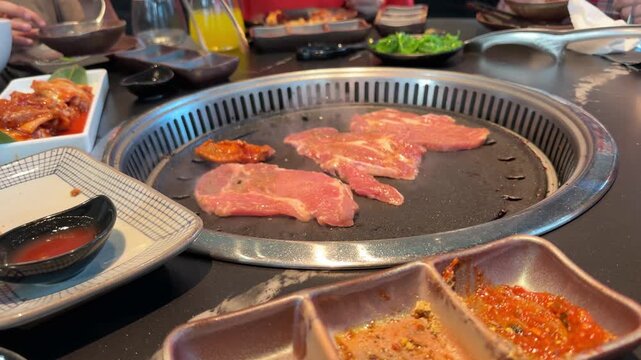 Raw meat slices and chicken, beef and squid pieces cooking tabletop built in asian barbecue grill restaurant, grilling on hot metal plate, BBQ cooking process, Group friends enjoying delicious food