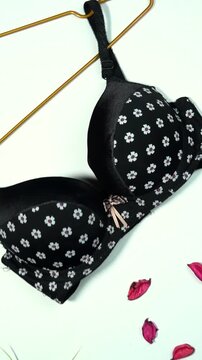 Black push-up bra with white daisy pattern on golden hanger and scattered red petals lingerie underwear fashion clothing apparel lingerie underwear fashion clothing apparel
