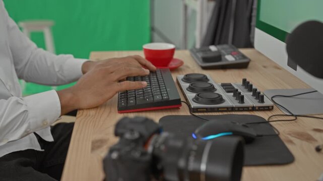 Man typing on keyboard with hands on keys at green screen studio table near red cup and camera; concentration creativity productivity.