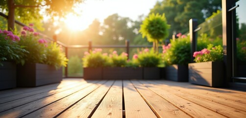 Fototapeta premium Warm sun shines on wooden deck with potted pink flowers and green shrubs. Outdoor patio with garden plants and trees in background. Peaceful summer morning.