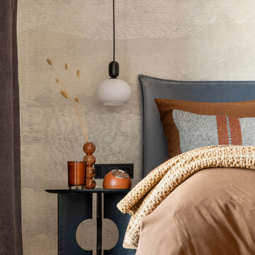 Stylish composition of modern bedroom interior. Bed, creative lamp and elegant personal accessories. Concrete wall. Brown sheeets. Minimalistic masculine concept. Template.