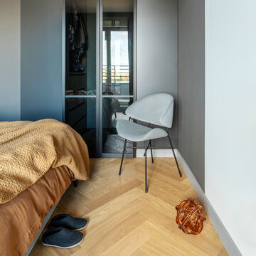 Stylish composition of modern bedroom interior. Wardrobe , grey chair and elegant personal accessories. Grey wall. Brown sheeets. Minimalistic masculine concept. Template.