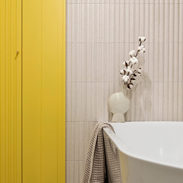 Minimalist bathroom interior with a freestanding white bathtub, a cotton plant in a vase, and a vibrant yellow cupboard