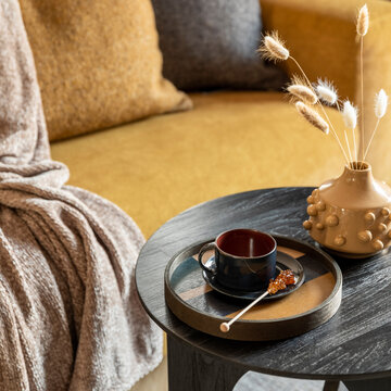 Cozy living room interior with a warm yellow sofa, decorative pillows, a textured throw, and a stylish side table featuring a cup and decor