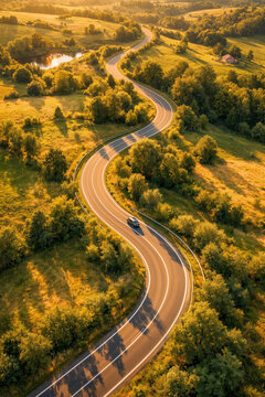 Curving rural road crossing sunlit green and gold fields from above, peaceful aerial view of countryside travel, open landscape and summer scenery.